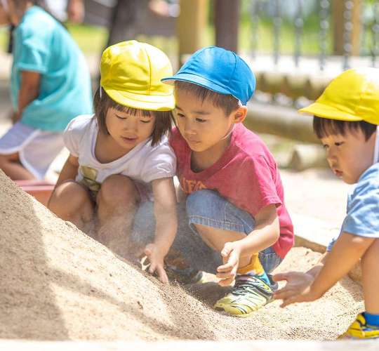 3人の園児が砂場で山を作って遊んでいる写真