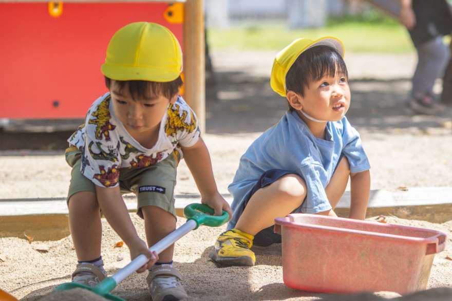 2人の男の子が砂場でスコップとバケツを使って遊んでいる写真