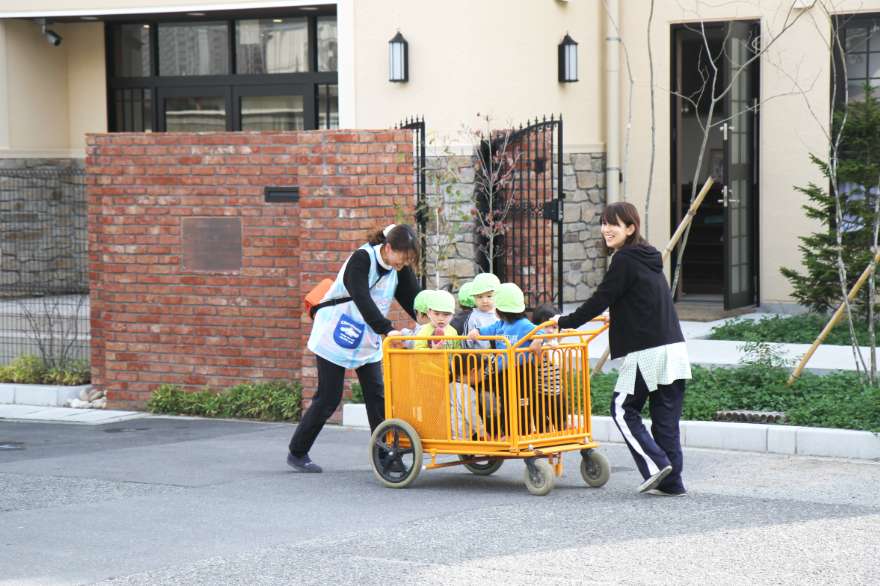 園児たちがお散歩カーを押す2人の先生の写真